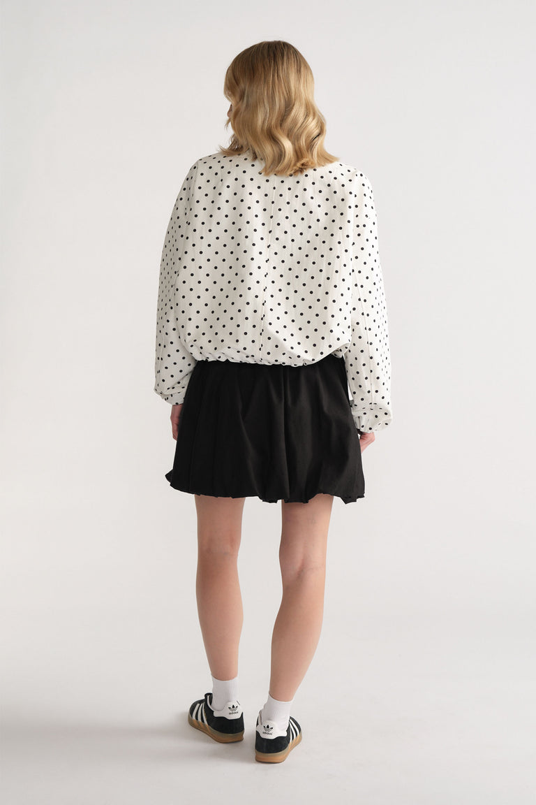Back view of woman wearing a black bubble mini skirt paired with a loose white polka dot blouse and sneakers