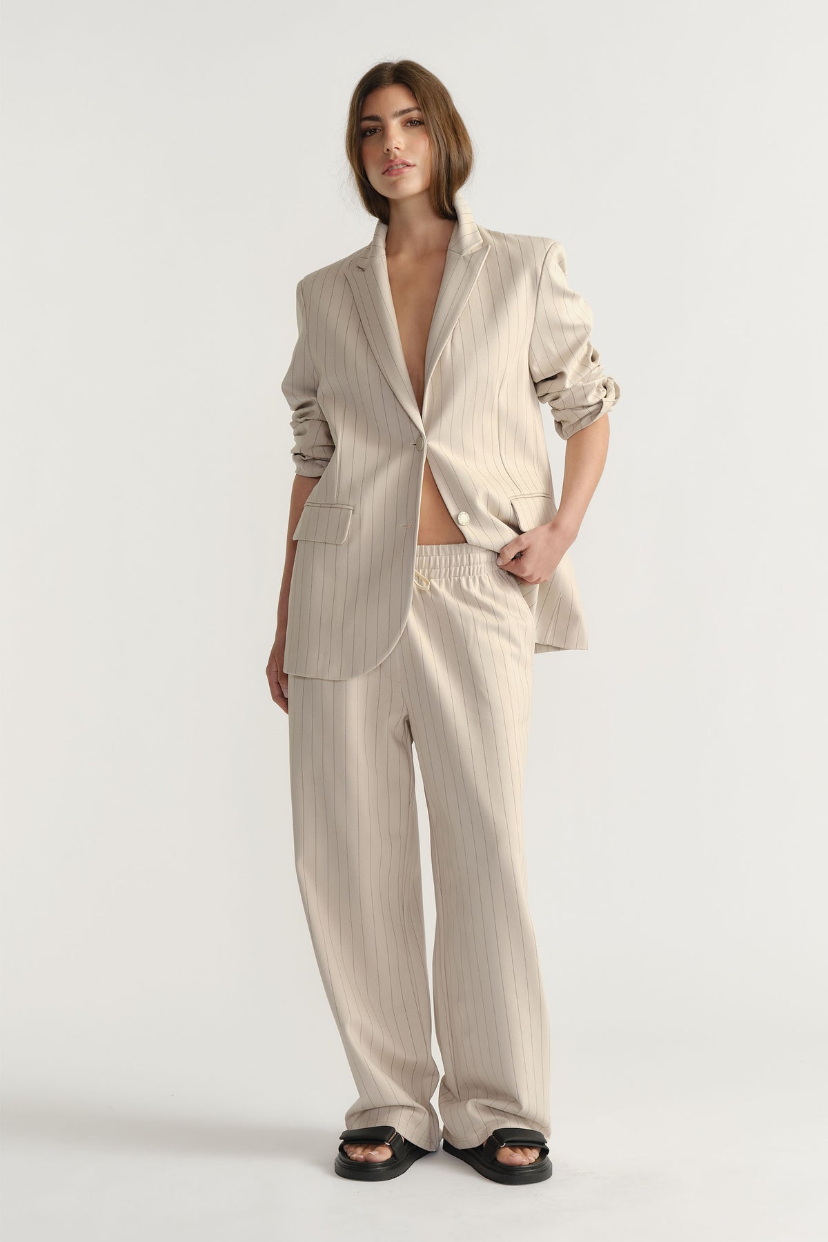 Woman wearing D-Luxe Pinstripe Blazer in light beige with rolled sleeves, paired with matching relaxed pants by Decjuba Australian brand