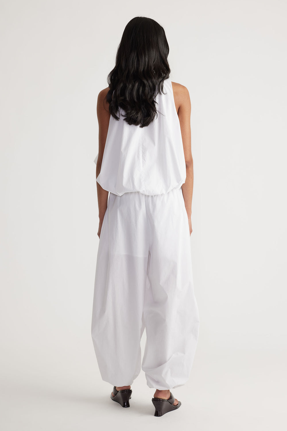 Back view of woman wearing relaxed white cotton balloon pants paired with a sleeveless top and black heeled sandals