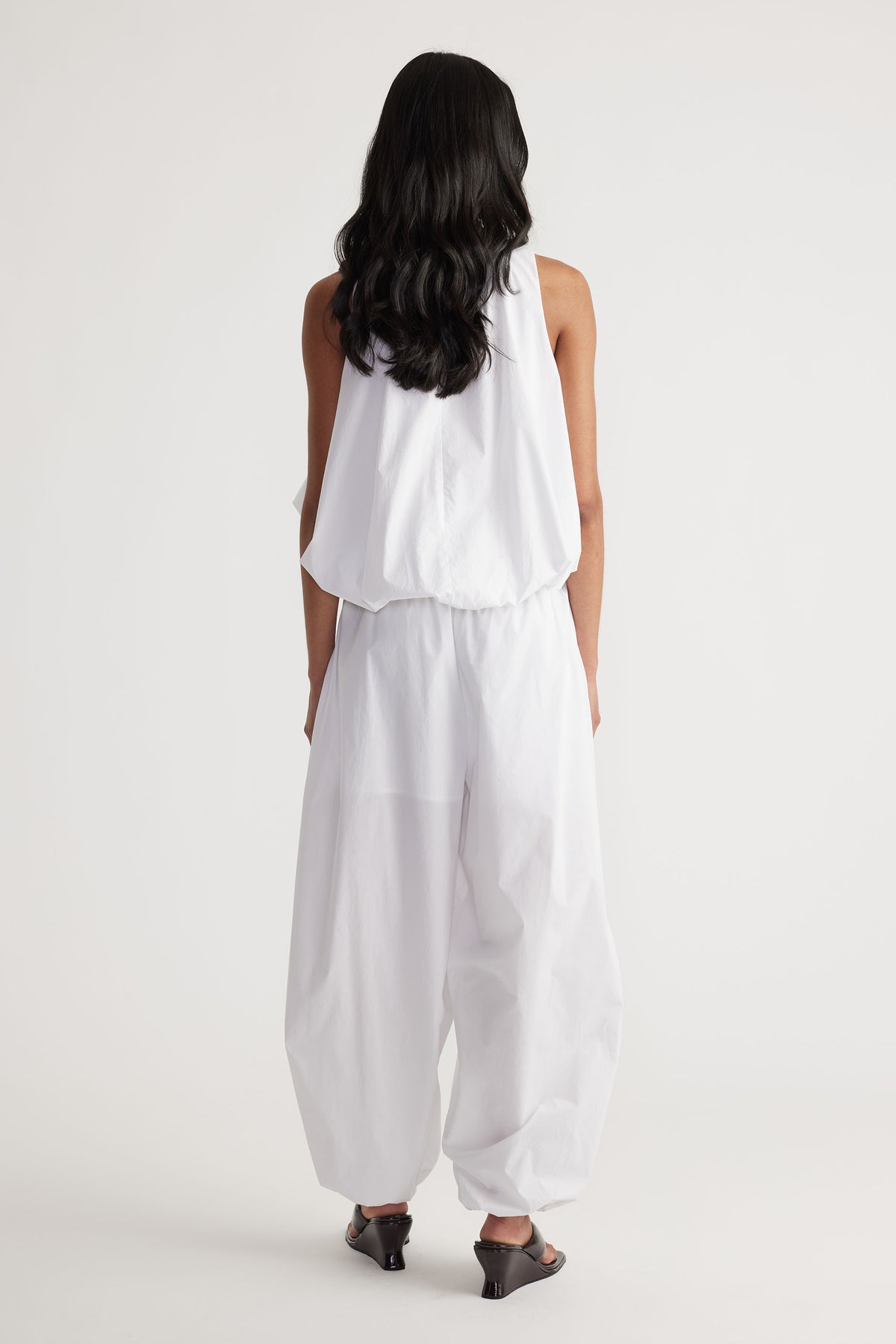 Back view of woman wearing relaxed white cotton balloon pants paired with a sleeveless top and black heeled sandals