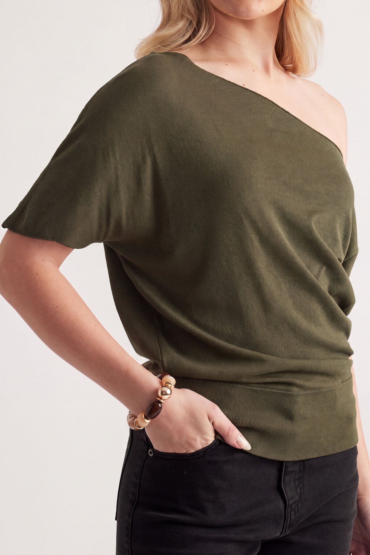 Woman wearing olive green off-shoulder top with relaxed fit, accessorized with a neutral beaded stretch bracelet