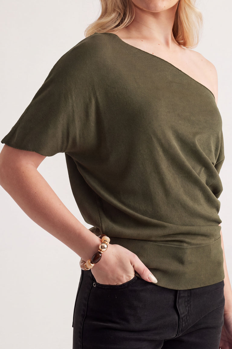 Woman wearing olive green off-shoulder top with relaxed fit, accessorized with a neutral beaded stretch bracelet