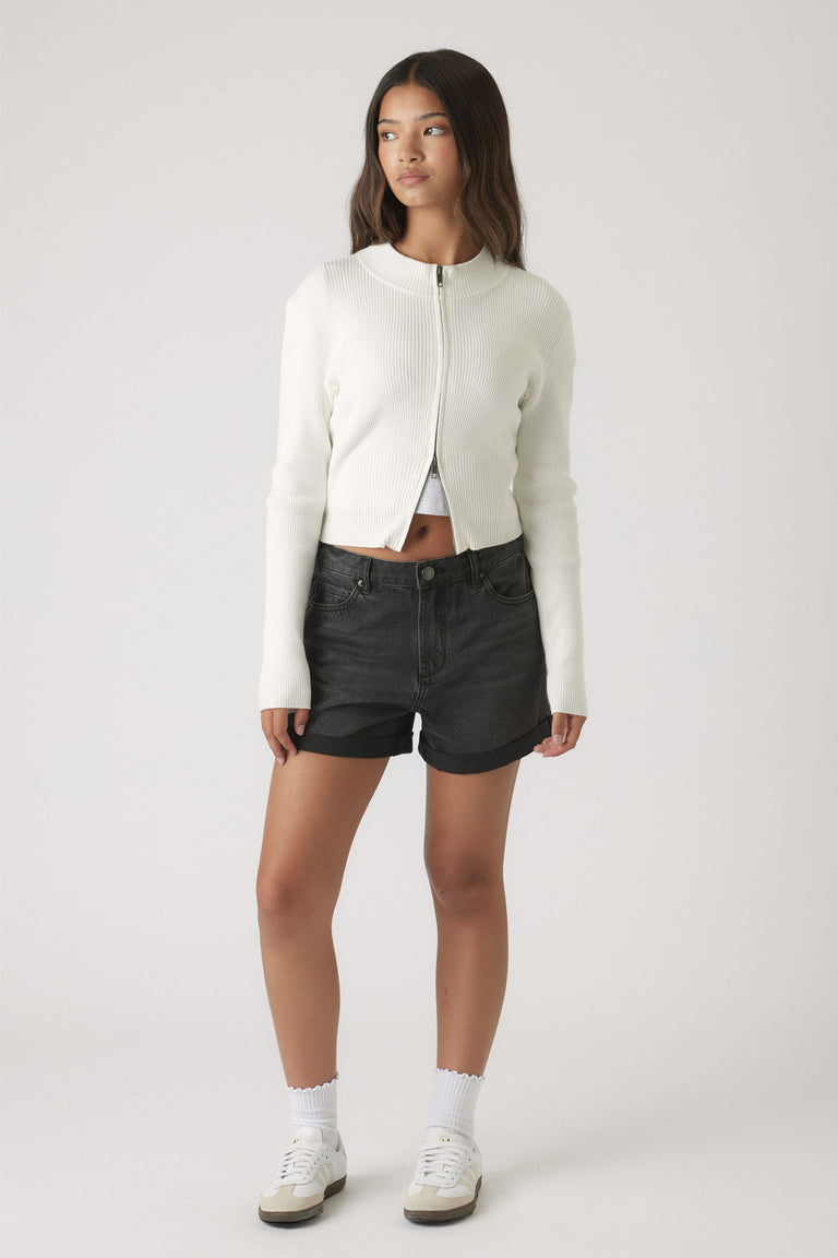 Teen girl wearing a cropped white zip-up sweater and black denim cuffed shorts for casual, effortless style.