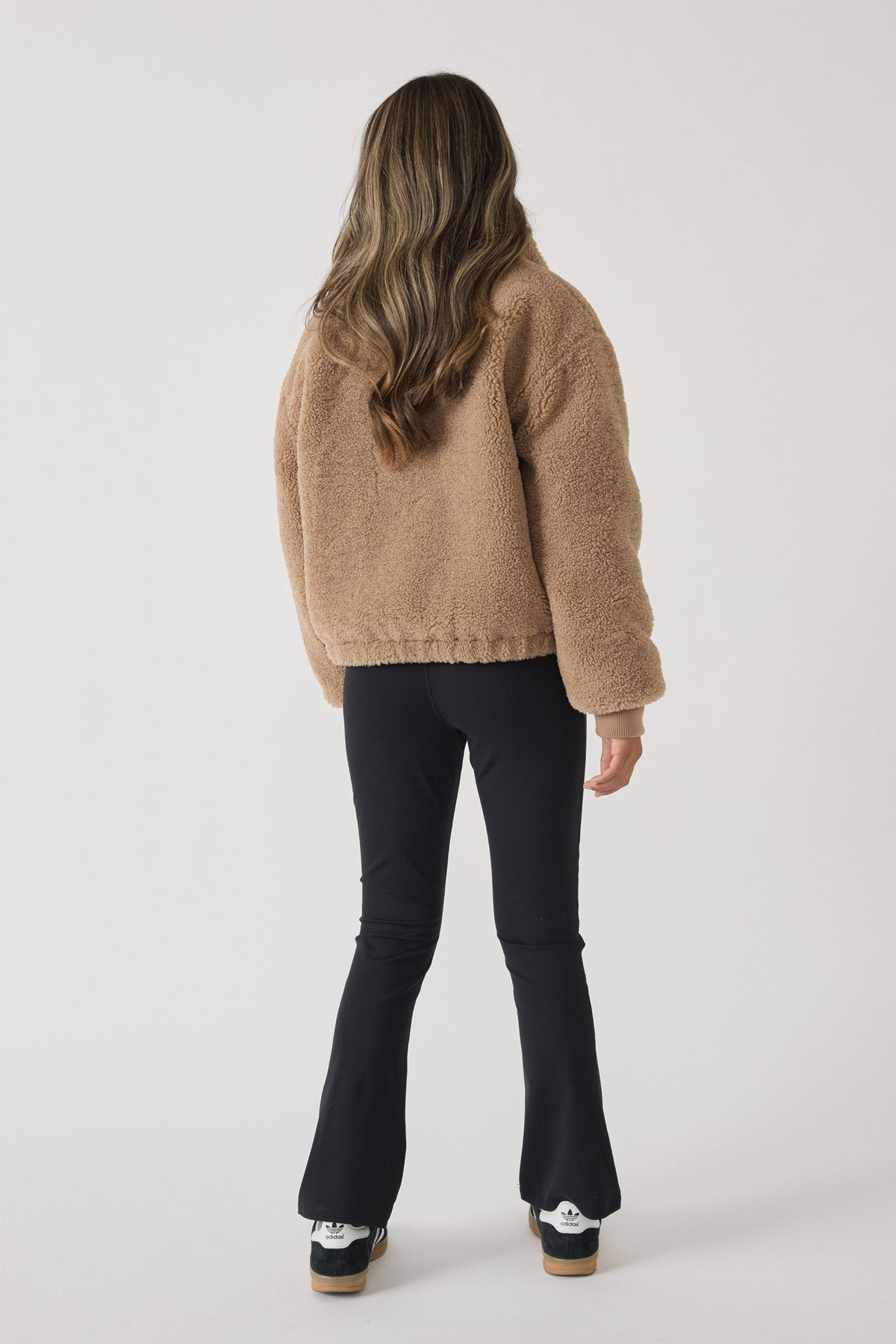 Girl wearing black stretchy yoga pants with a slightly flared leg, paired with a cozy tan fleece jacket.