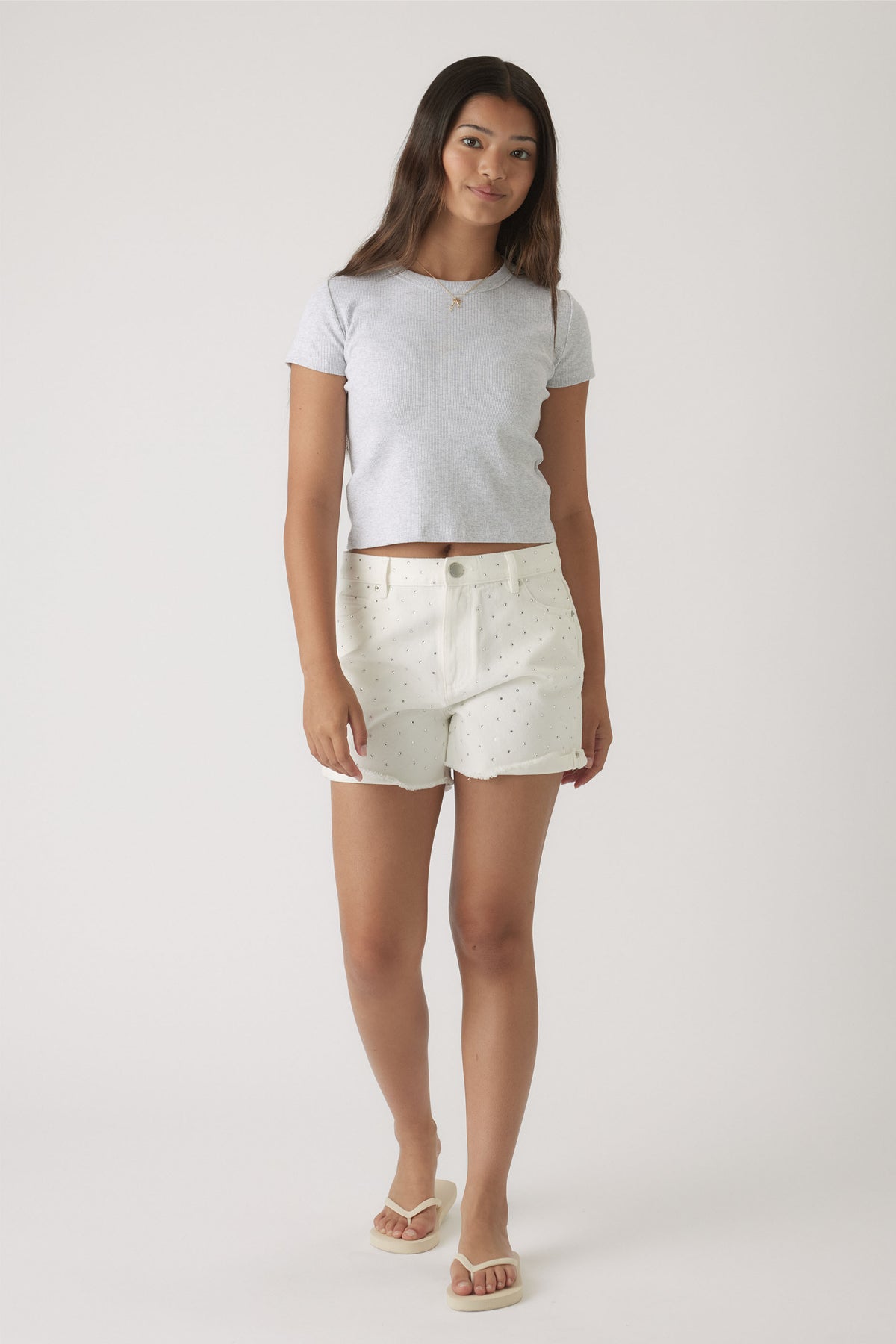 Teen girl wearing white denim shorts with subtle rhinestone details and a fitted light grey short sleeve top