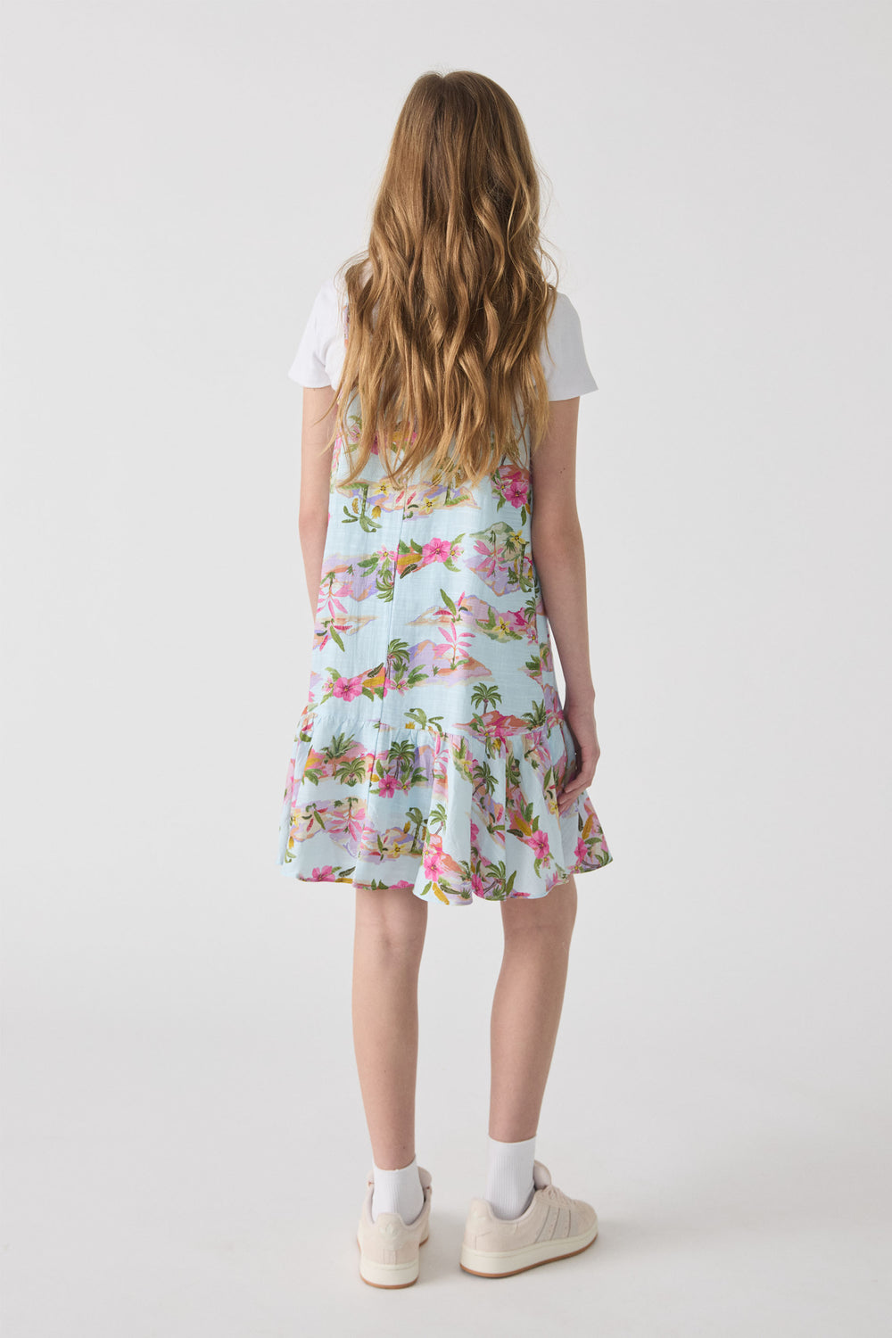 Girl wearing a light blue tropical print strappy dress layered over a white tee, paired with white socks and sneakers.