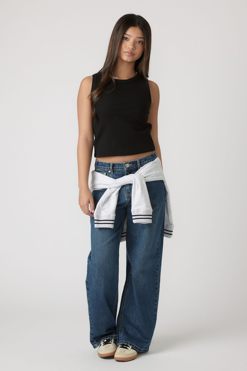 Teen girl wearing Girls Harper Logo Tank in black paired with relaxed blue denim jeans and white sweatshirt by Decjuba Australian brand