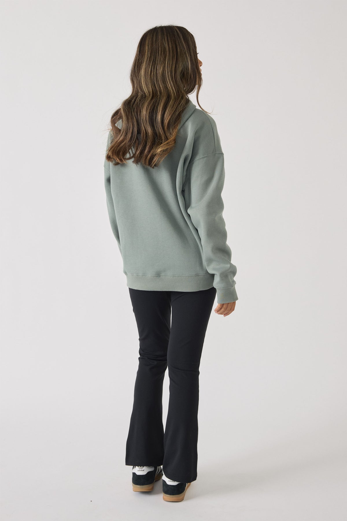Rear view of a girl wearing a sage green oversized hoodie paired with fitted black flare pants and sneakers