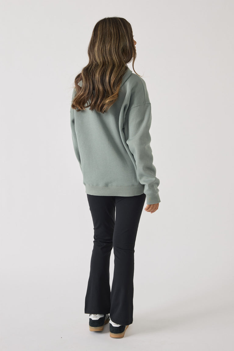 Rear view of a girl wearing a sage green oversized hoodie paired with fitted black flare pants and sneakers