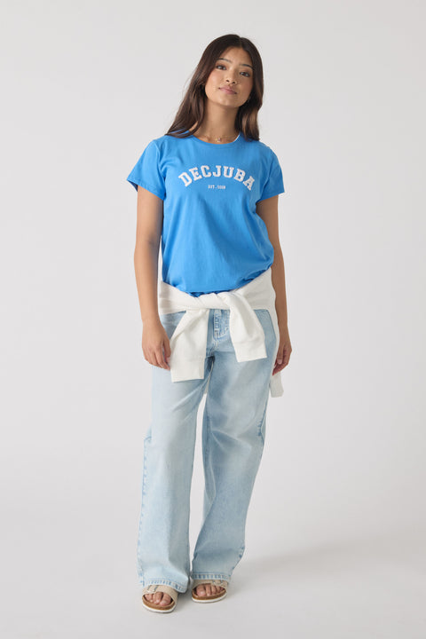 Teen girl wearing a bright blue logo tee paired with light wash wide-leg jeans and a white sweater tied at the waist.