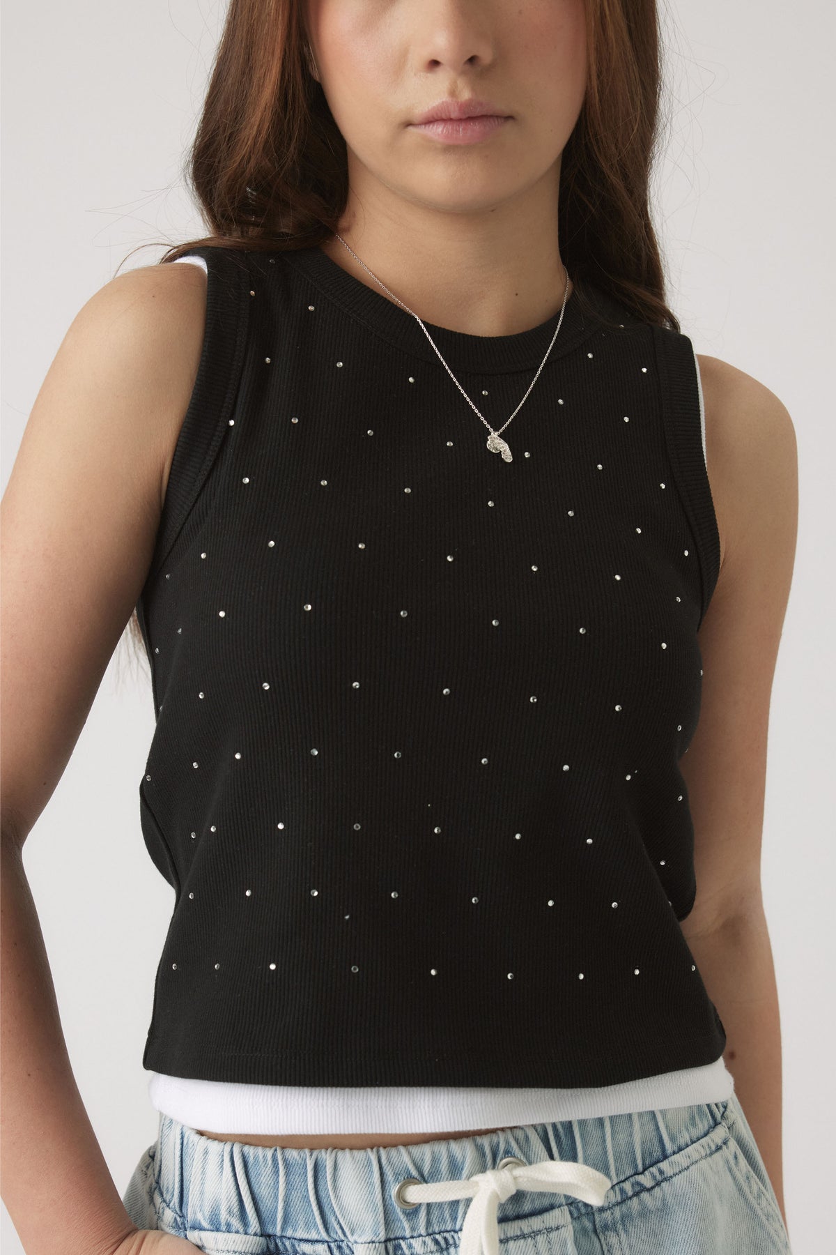 Girl wearing a black sleeveless tank top adorned with small crystal embellishments, paired with light denim shorts.