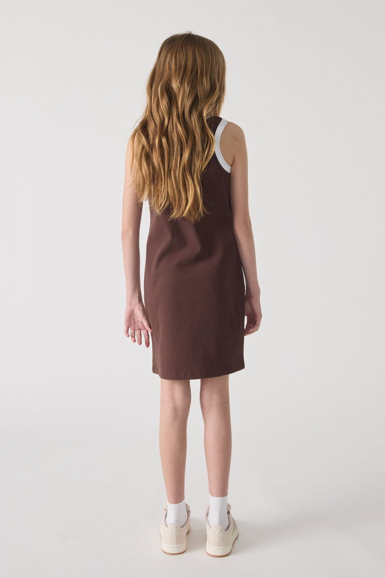 Girl seen from behind wearing a sleeveless chocolate brown dress with white trim and casual white sneakers