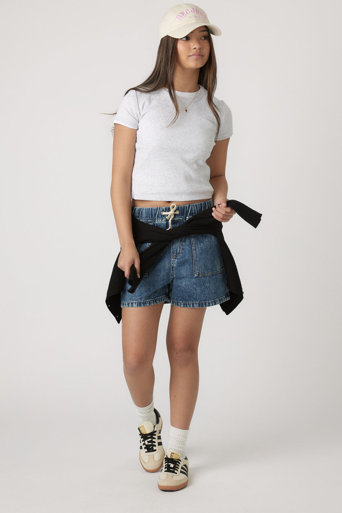 Teen girl styled in a light crop tee paired with relaxed denim shorts and casual sneakers for easy, everyday wear.