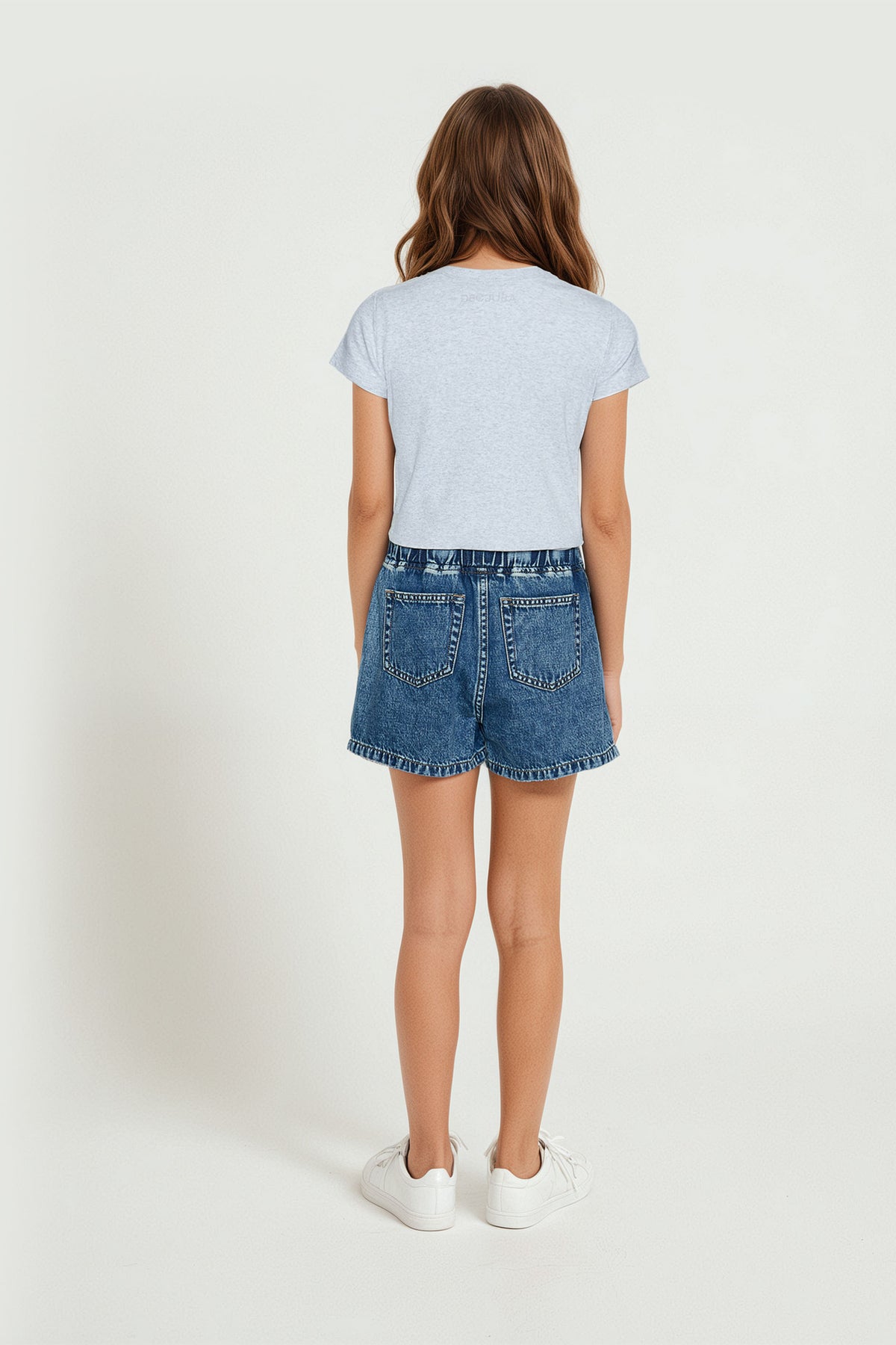 Young girl wearing a soft grey crop tee paired with relaxed denim shorts and white sneakers for casual comfort.