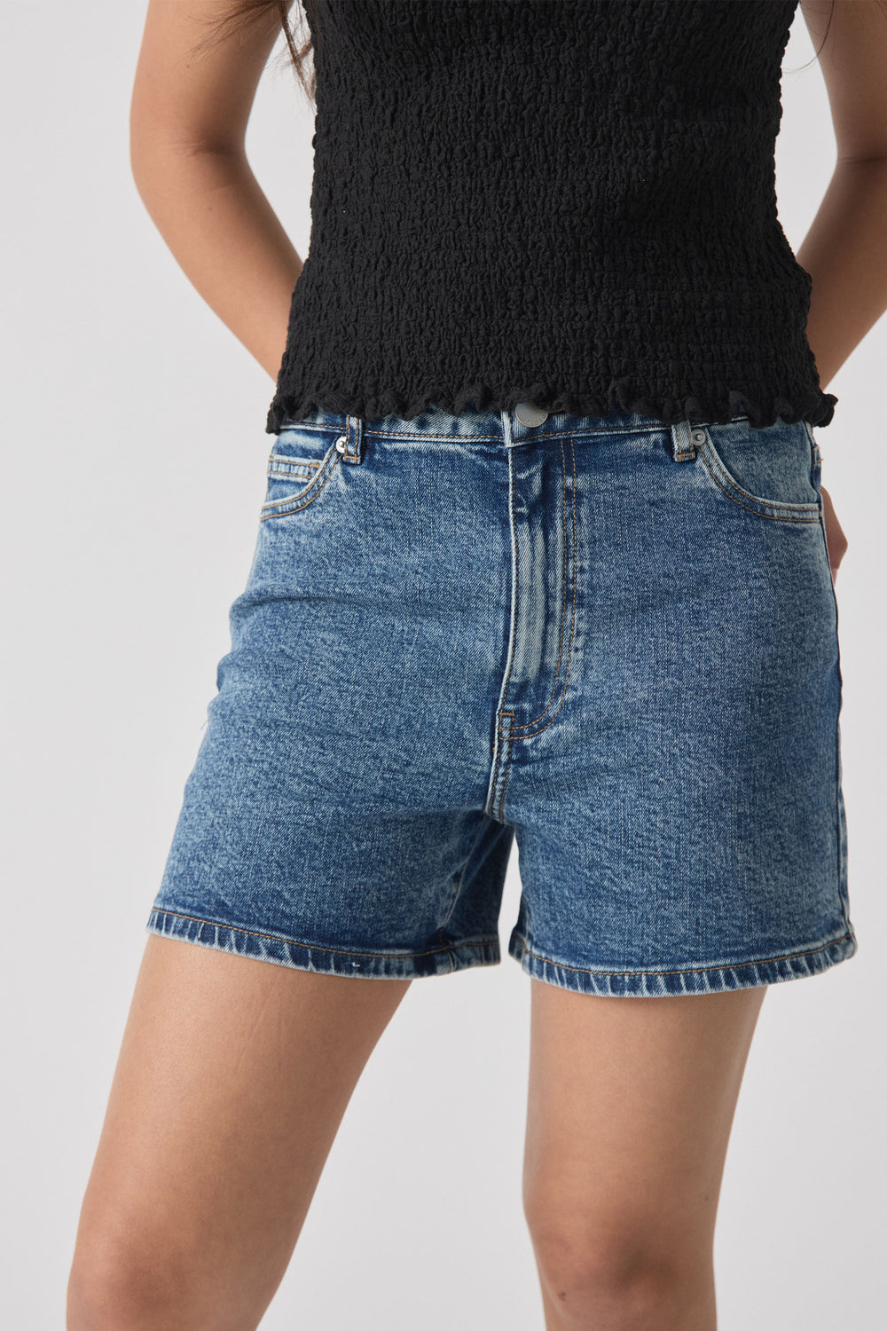 Close-up of girl wearing mid-rise blue denim shorts with rolled hems and a textured black sleeveless top