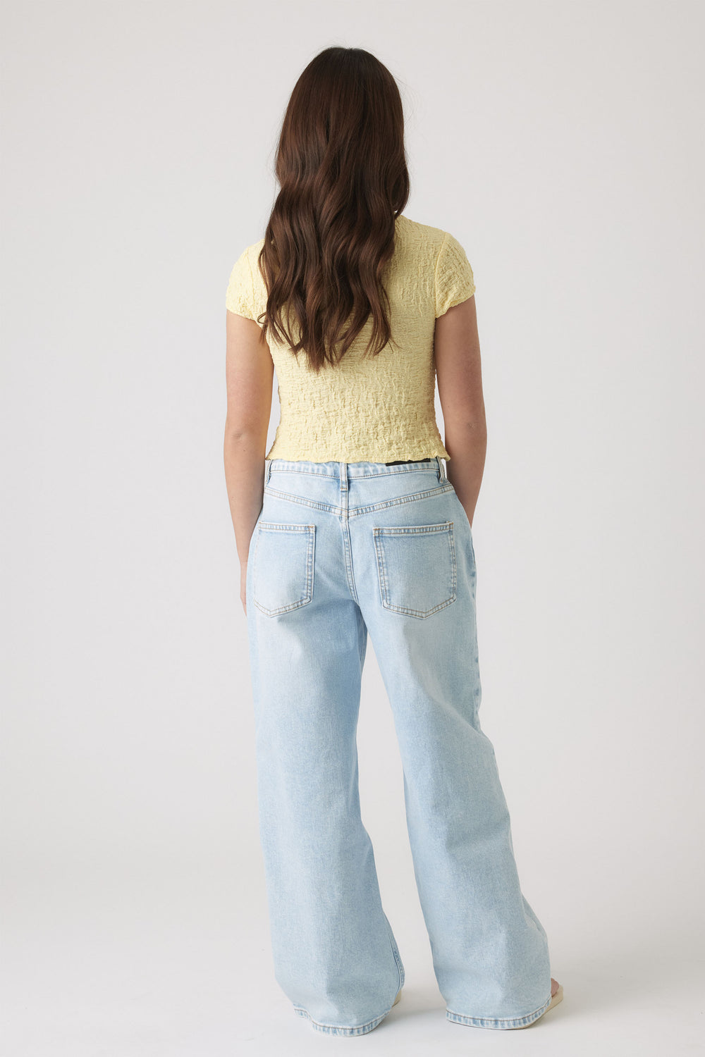 Back view of girl wearing a textured pale yellow top with short sleeves paired with light blue wide-leg jeans