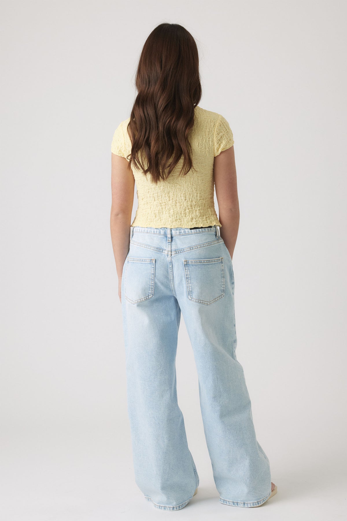 Back view of girl wearing a textured pale yellow top with short sleeves paired with light blue wide-leg jeans