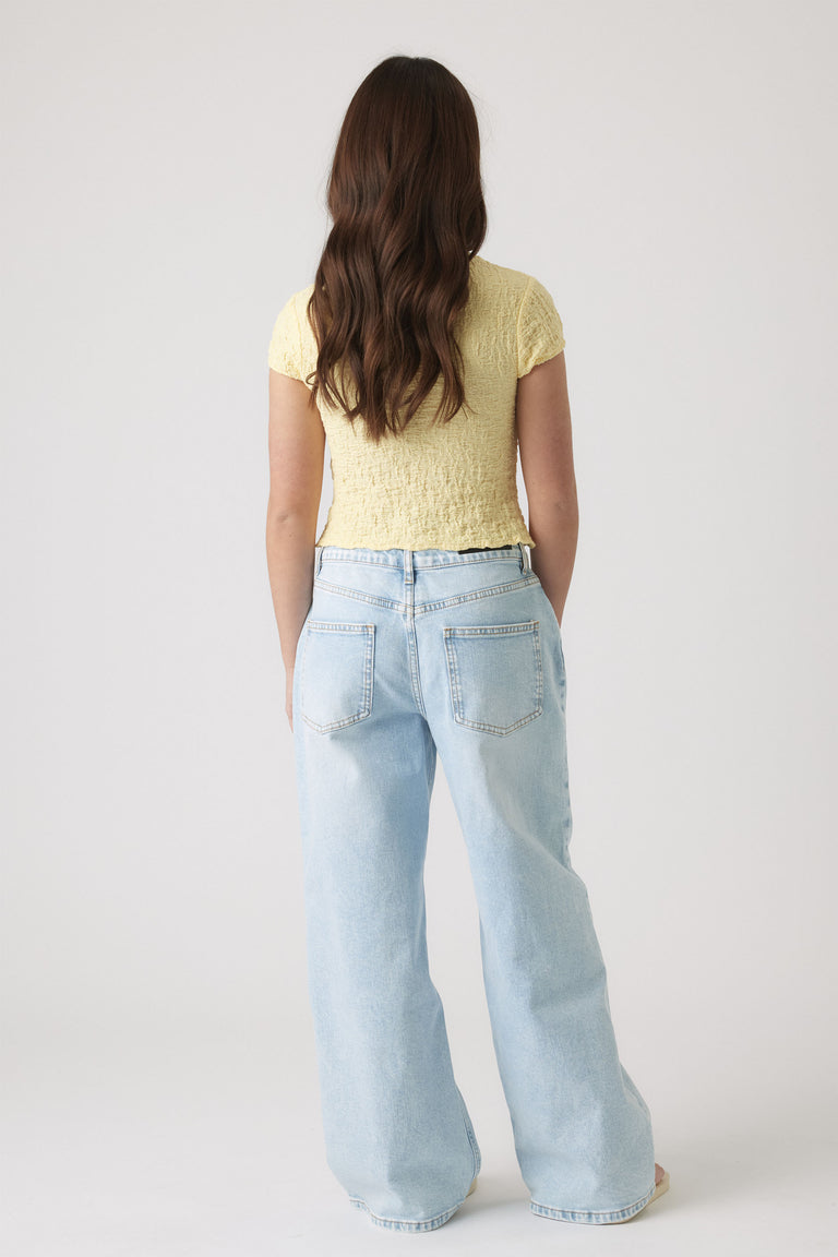 Back view of girl wearing a textured pale yellow top with short sleeves paired with light blue wide-leg jeans