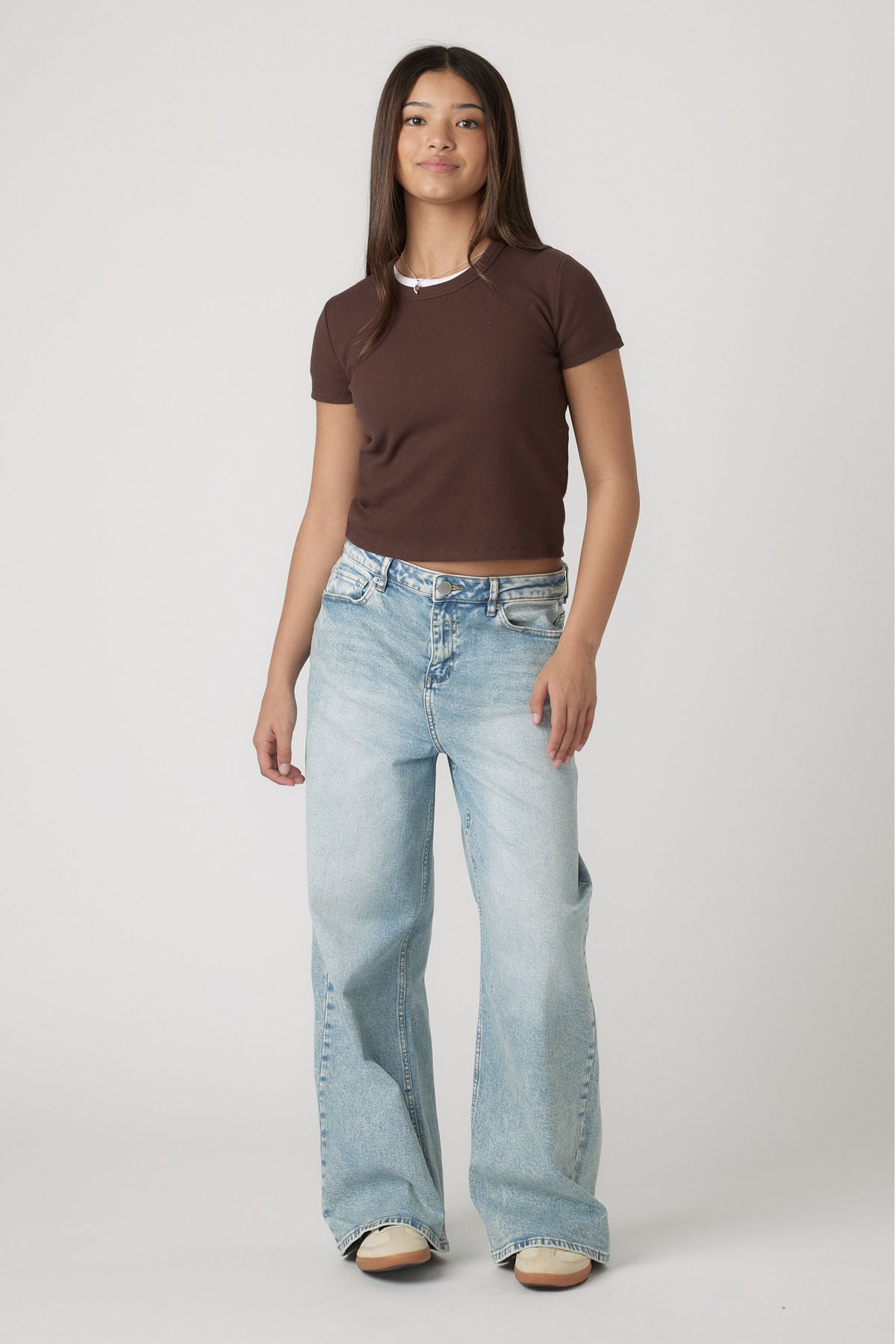 Teen girl wearing a fitted chocolate brown crop tee paired with light-wash wide-leg denim jeans and casual sneakers