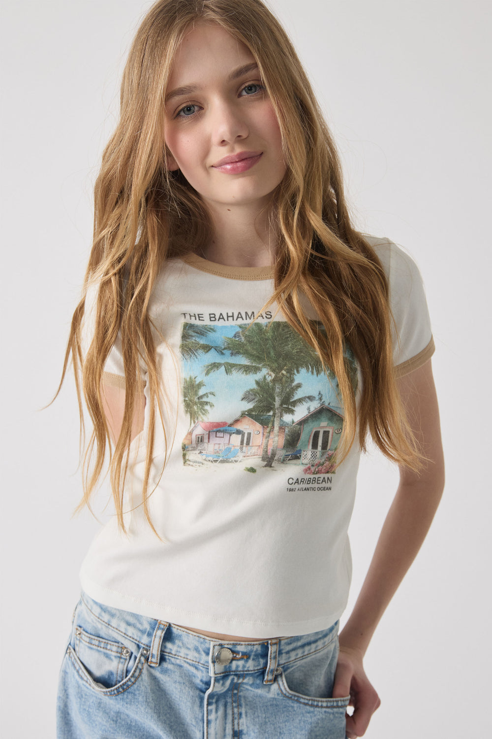 Girl wearing a cream crop tee with Bahamas print and contrast trim, paired with light wash denim jeans.