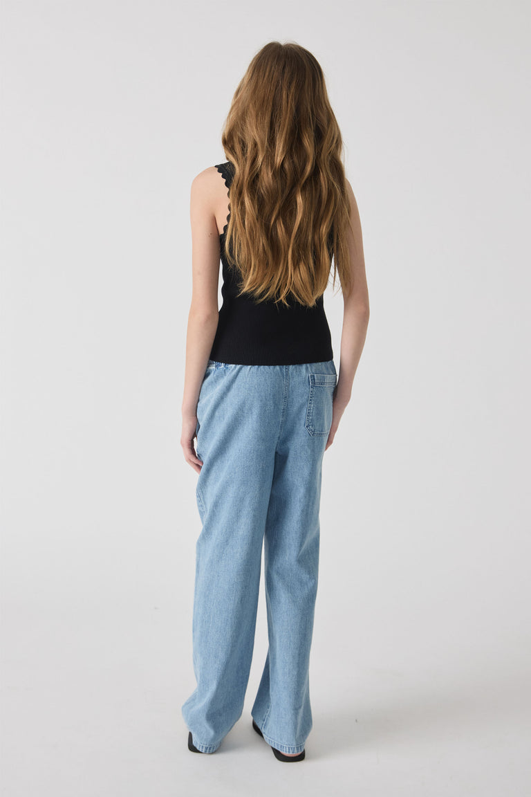 Girl wearing loose midwash denim pants paired with a black sleeveless top, viewed from the back.