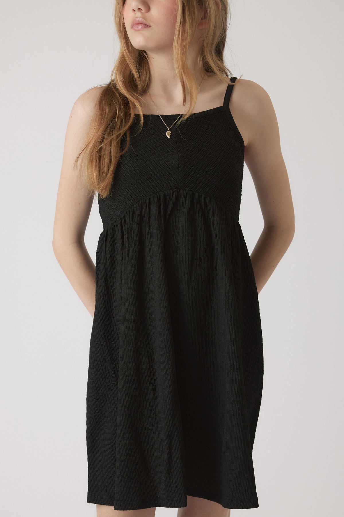 Girl wearing a black shirred dress with thin straps and relaxed skirt, paired with a delicate gold pendant necklace