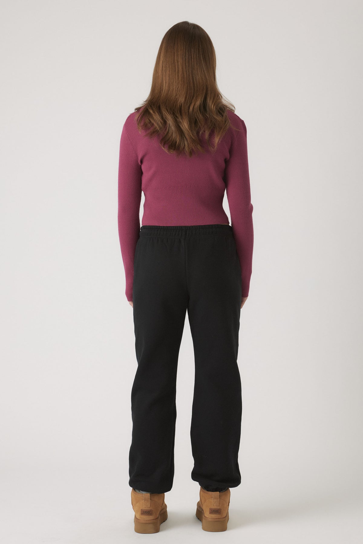 Back view of girl wearing black elastic cuff track pants paired with a fitted long sleeve top and tan boots