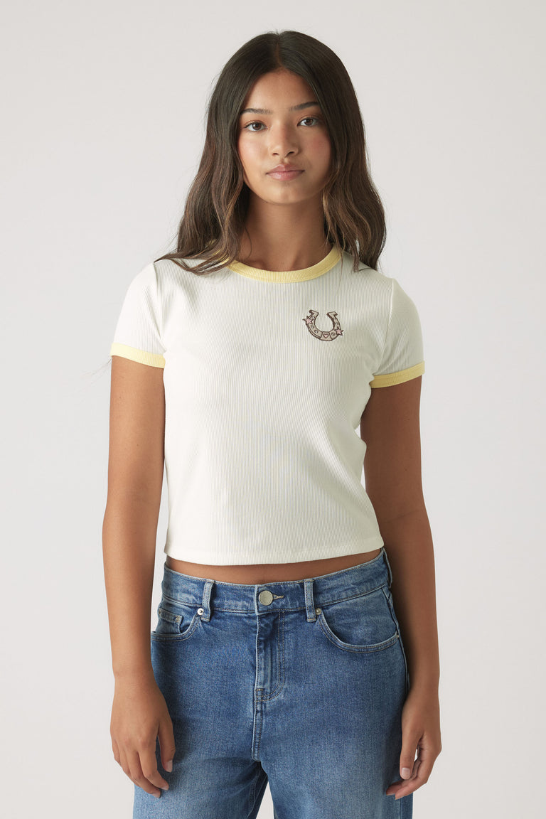 Girl wearing a white cropped ringer tee with yellow trim and embroidered design paired with relaxed blue denim jeans