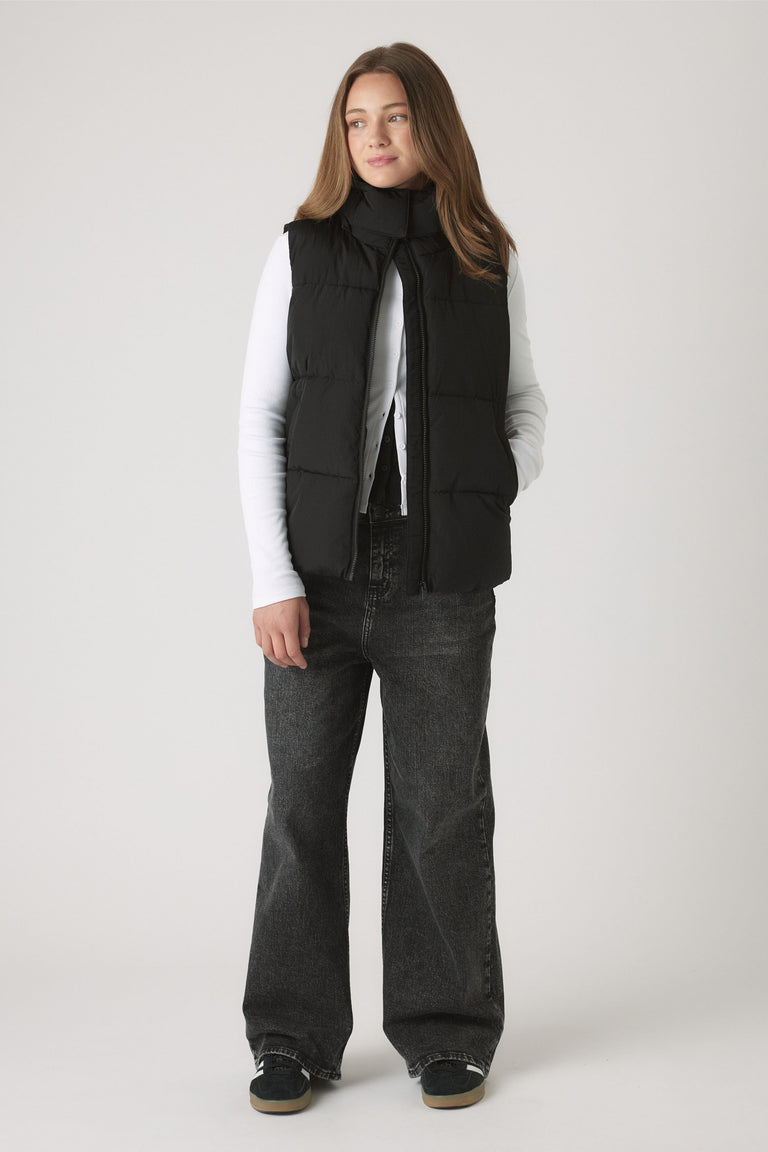 Girl wearing black Girls Hooded Puffer Vest over white long sleeve top and wide-leg jeans for a casual look