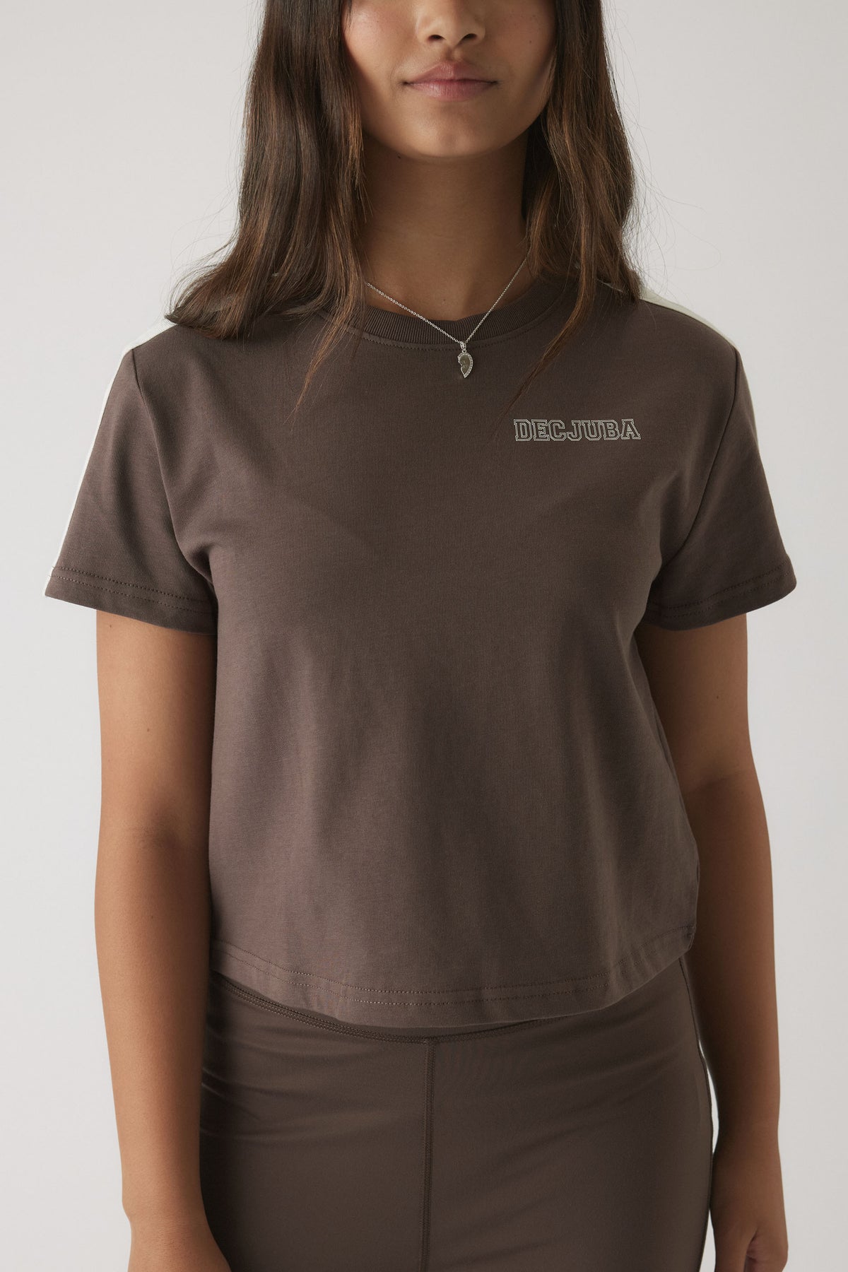 Girl wearing a relaxed fit mocha brown boxy tee with short sleeves and subtle brand logo detail on the chest