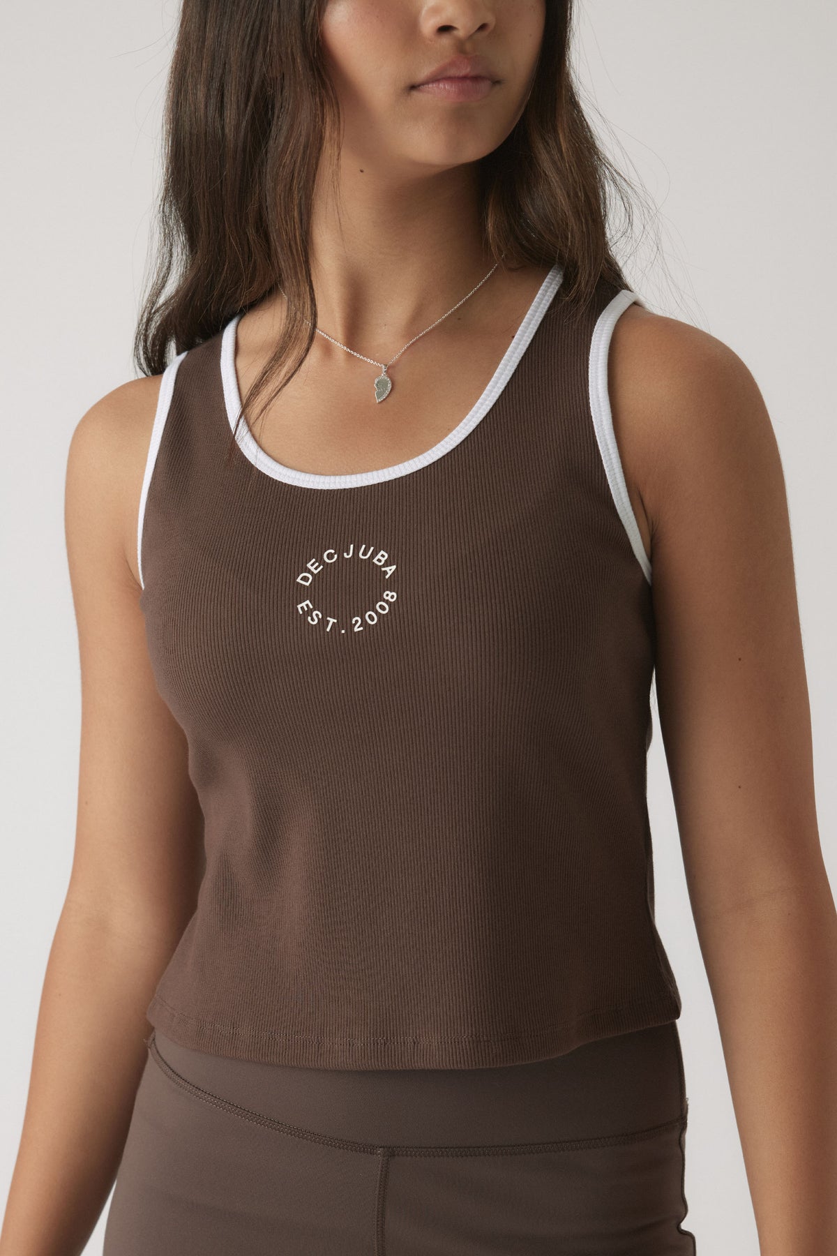 Close-up of a girl wearing a mocha brown cropped tank with contrasting white trim and subtle front logo detail.