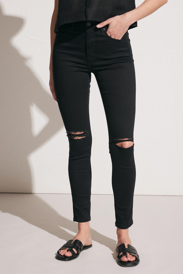 Woman wearing black distressed skinny jeans paired with black slide sandals against a neutral background