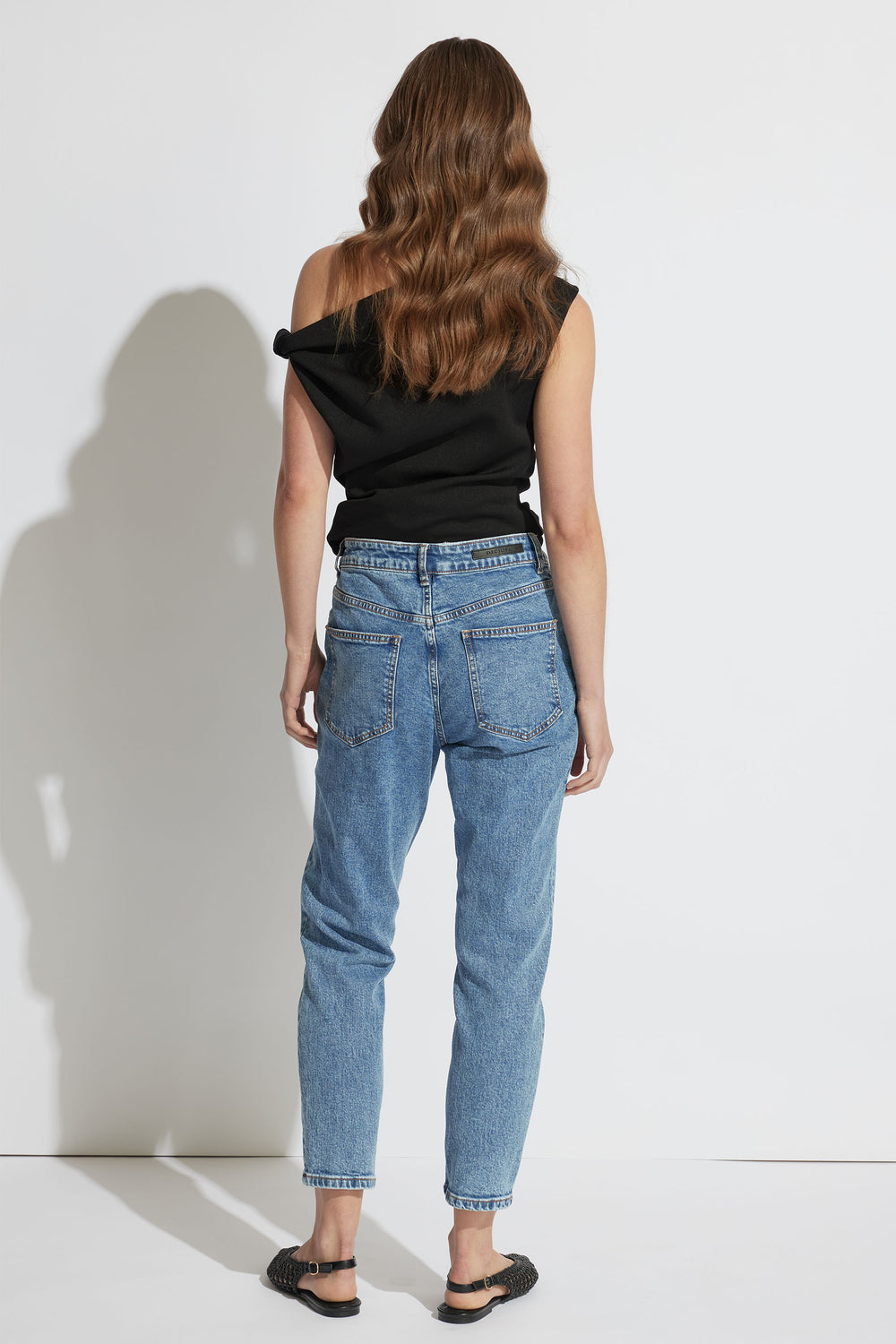 Woman wearing light blue high-rise relaxed fit jeans paired with a black sleeveless top and black woven sandals