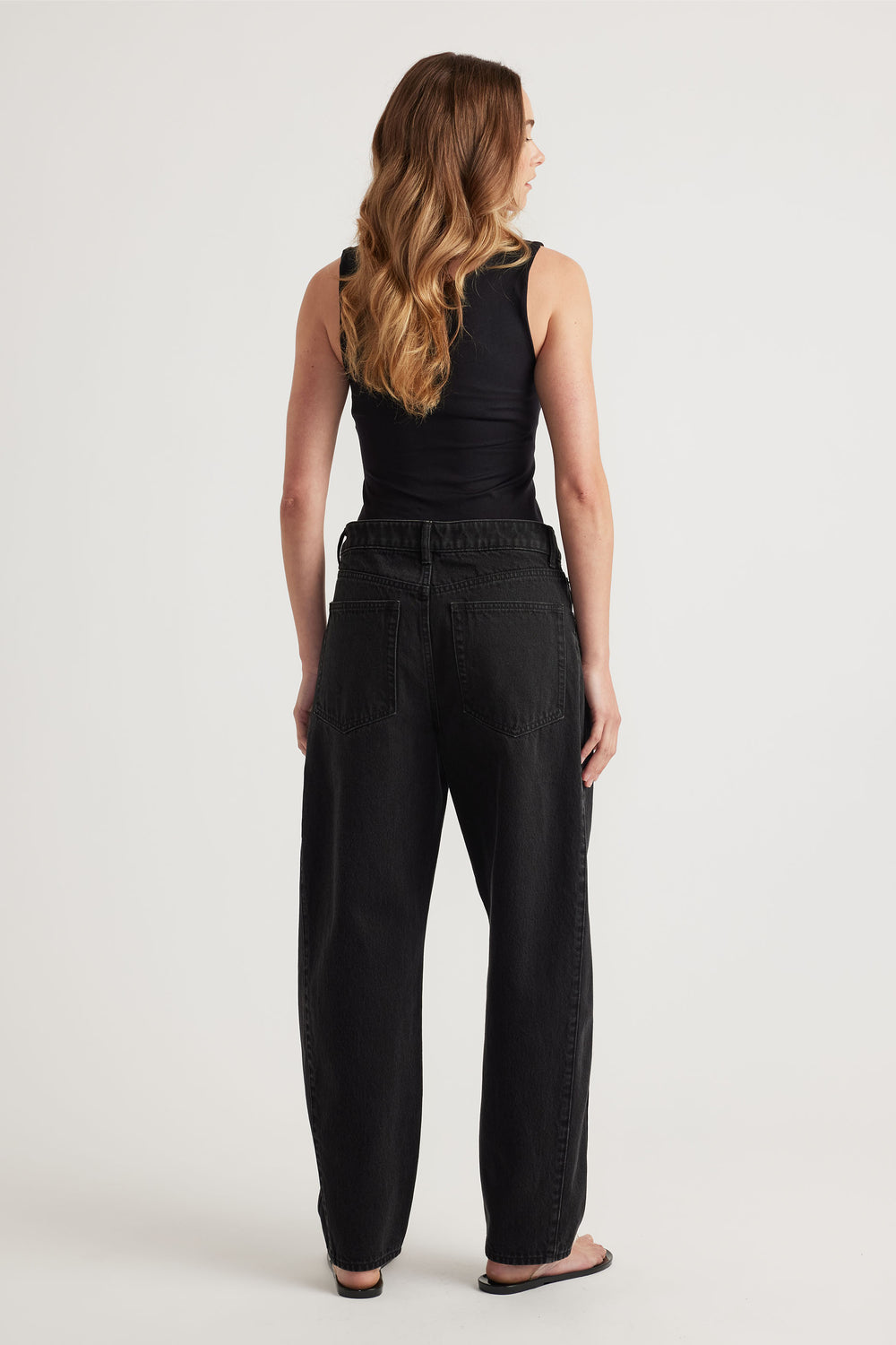 Woman wearing a black seamless scoop tank paired with relaxed fit high-waisted black denim jeans and sandals.