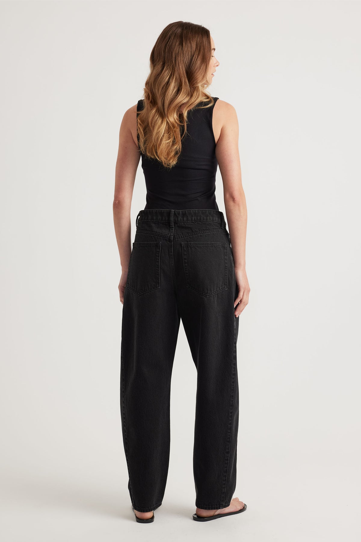 Woman wearing a black seamless scoop tank paired with relaxed fit high-waisted black denim jeans and sandals.