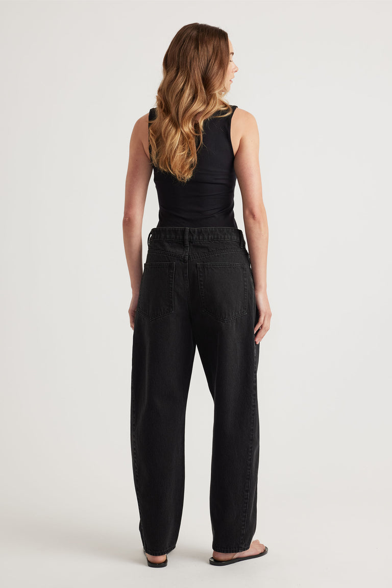 Woman wearing a black seamless scoop tank paired with relaxed fit high-waisted black denim jeans and sandals.