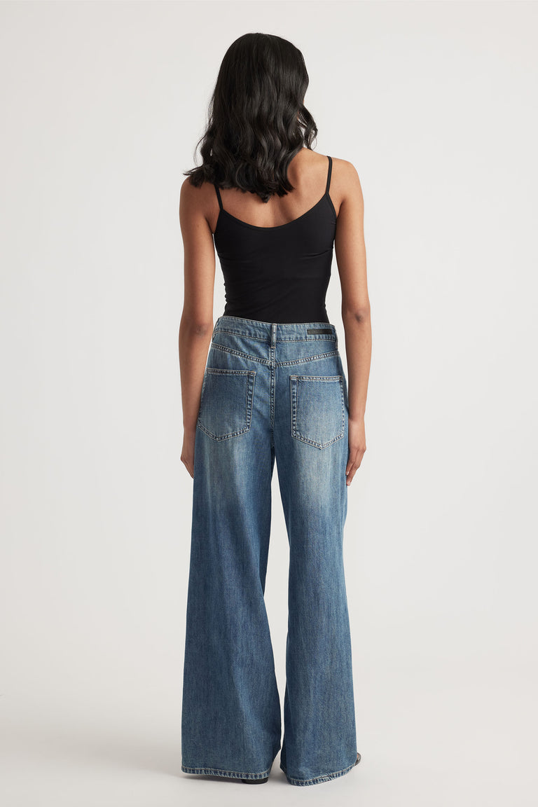 Back view of woman wearing wide-leg blue denim jeans paired with a black seamless thin strap tank top
