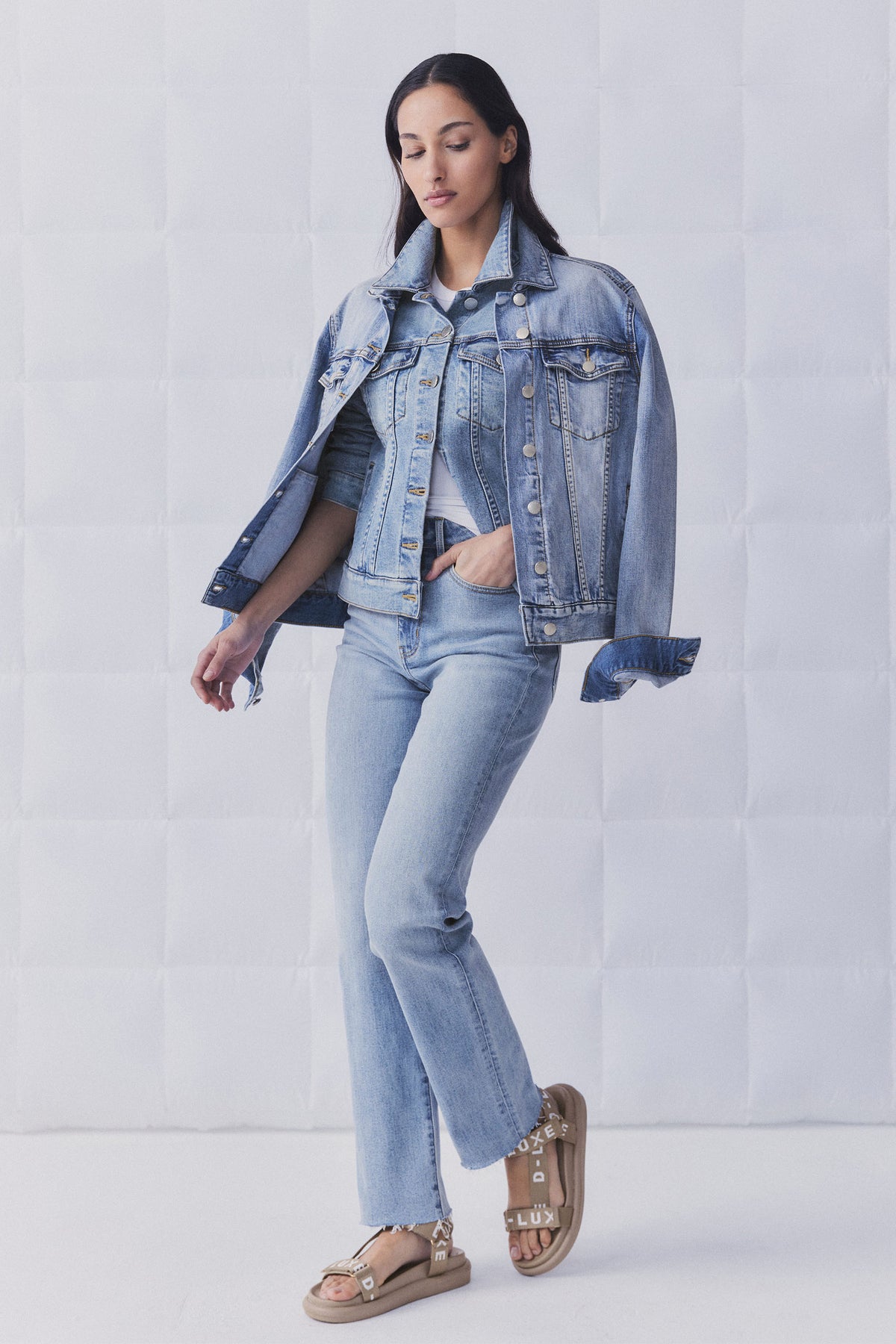 Woman wearing light blue straight leg jeans with a matching denim jacket draped over shoulders for a relaxed look
