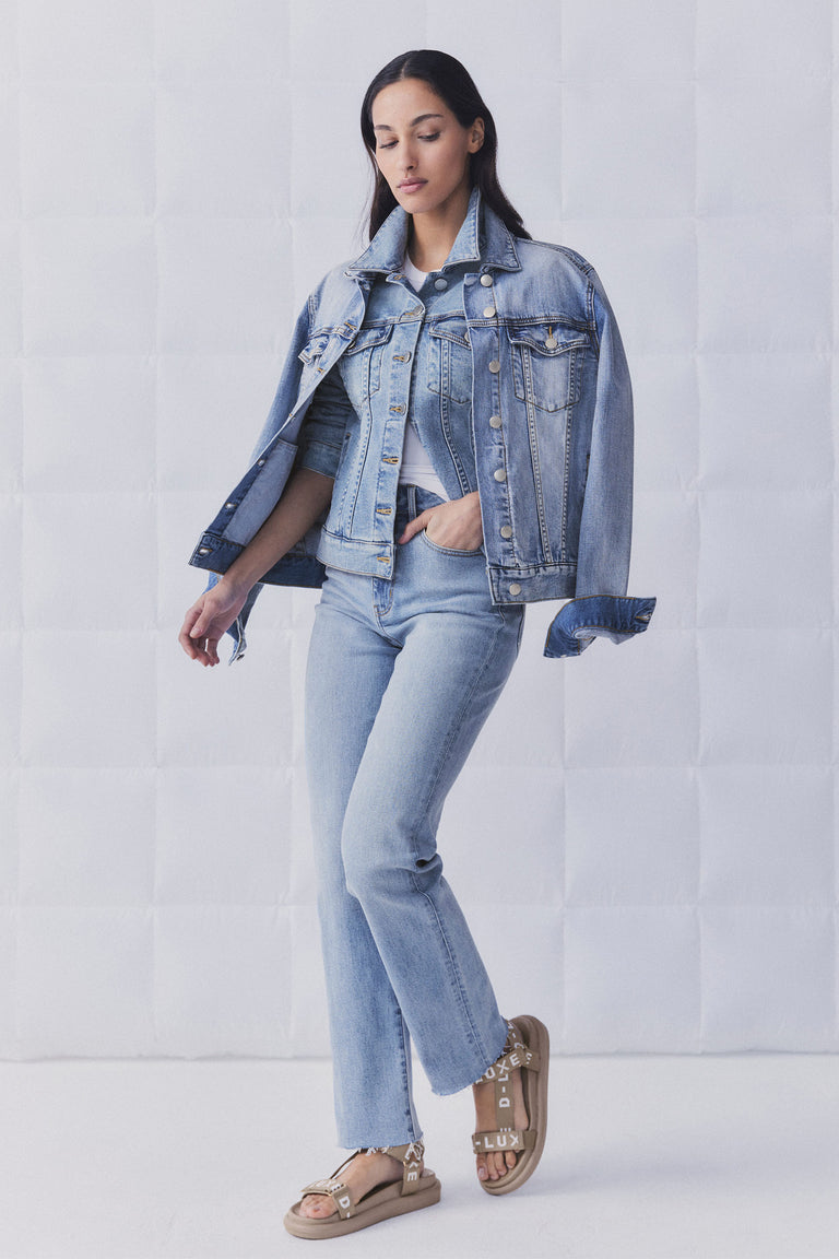 Woman wearing light blue straight leg jeans with a matching denim jacket draped over shoulders for a relaxed look