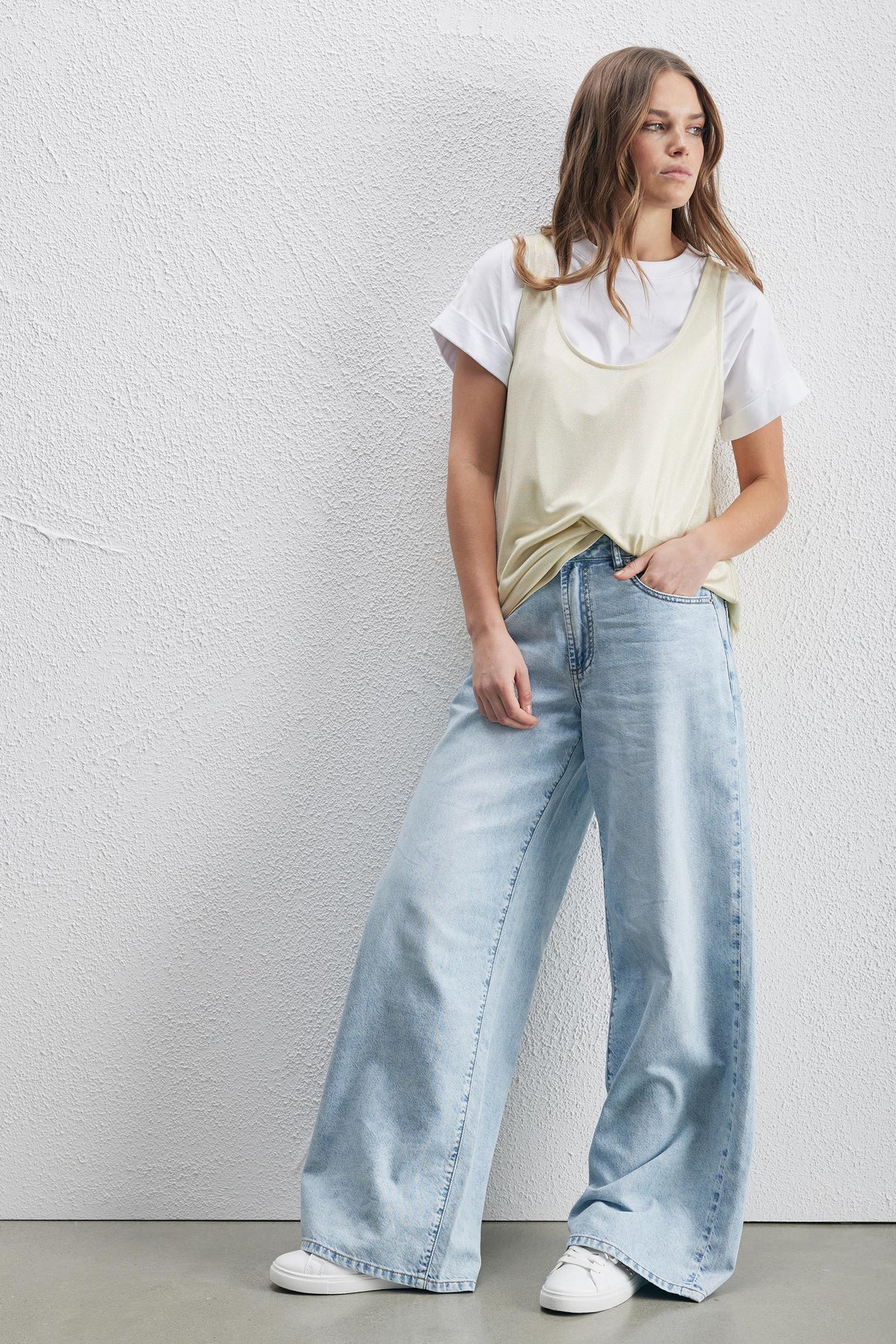 Woman wearing a pale metallic tank top over a white tee with wide leg jeans and sneakers