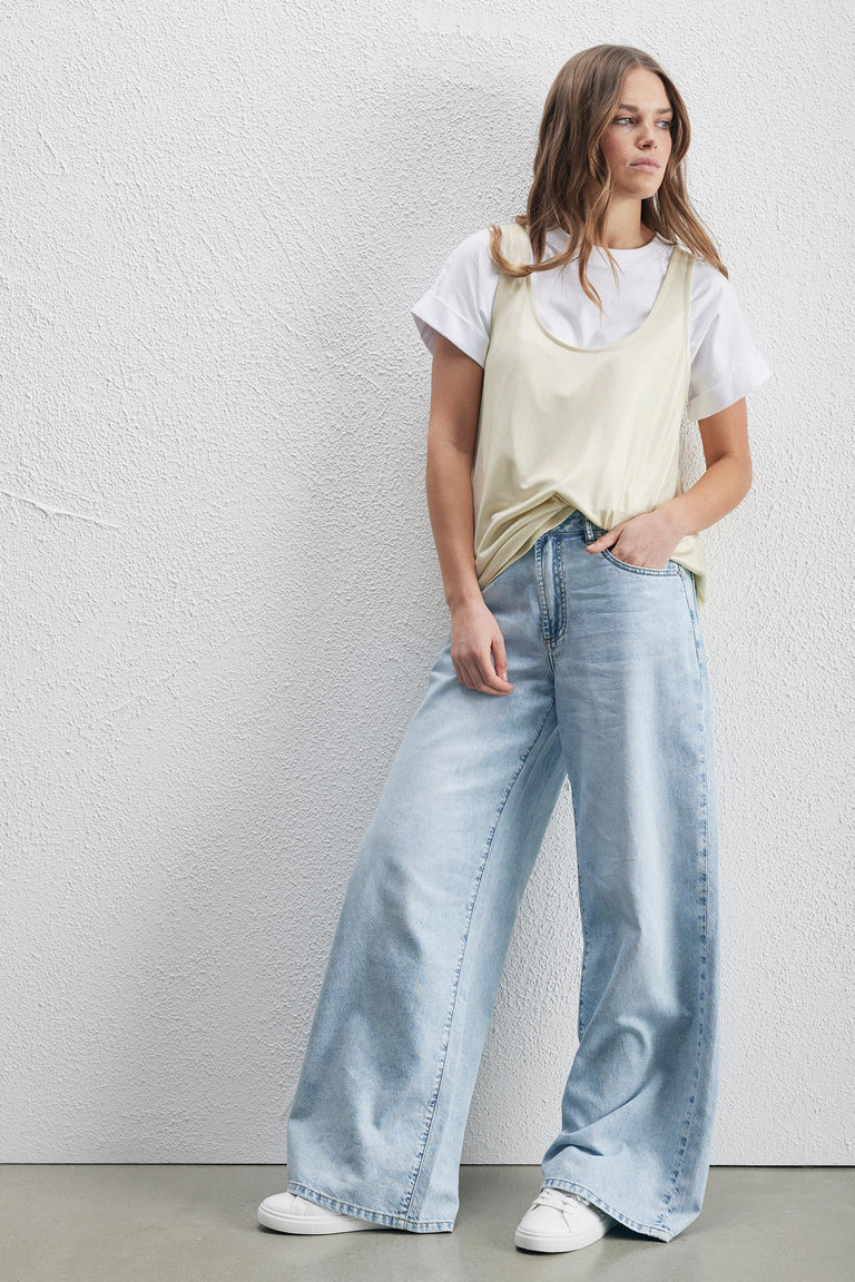 Woman wearing a pale metallic tank top over a white tee with wide leg jeans and sneakers