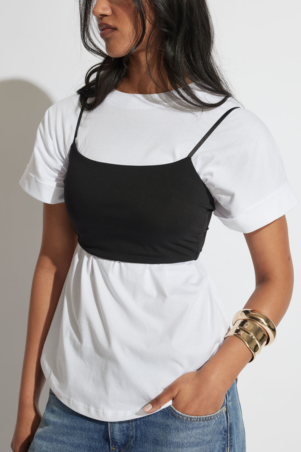 Woman wearing a black fitted crop top over a white T shirt with blue jeans