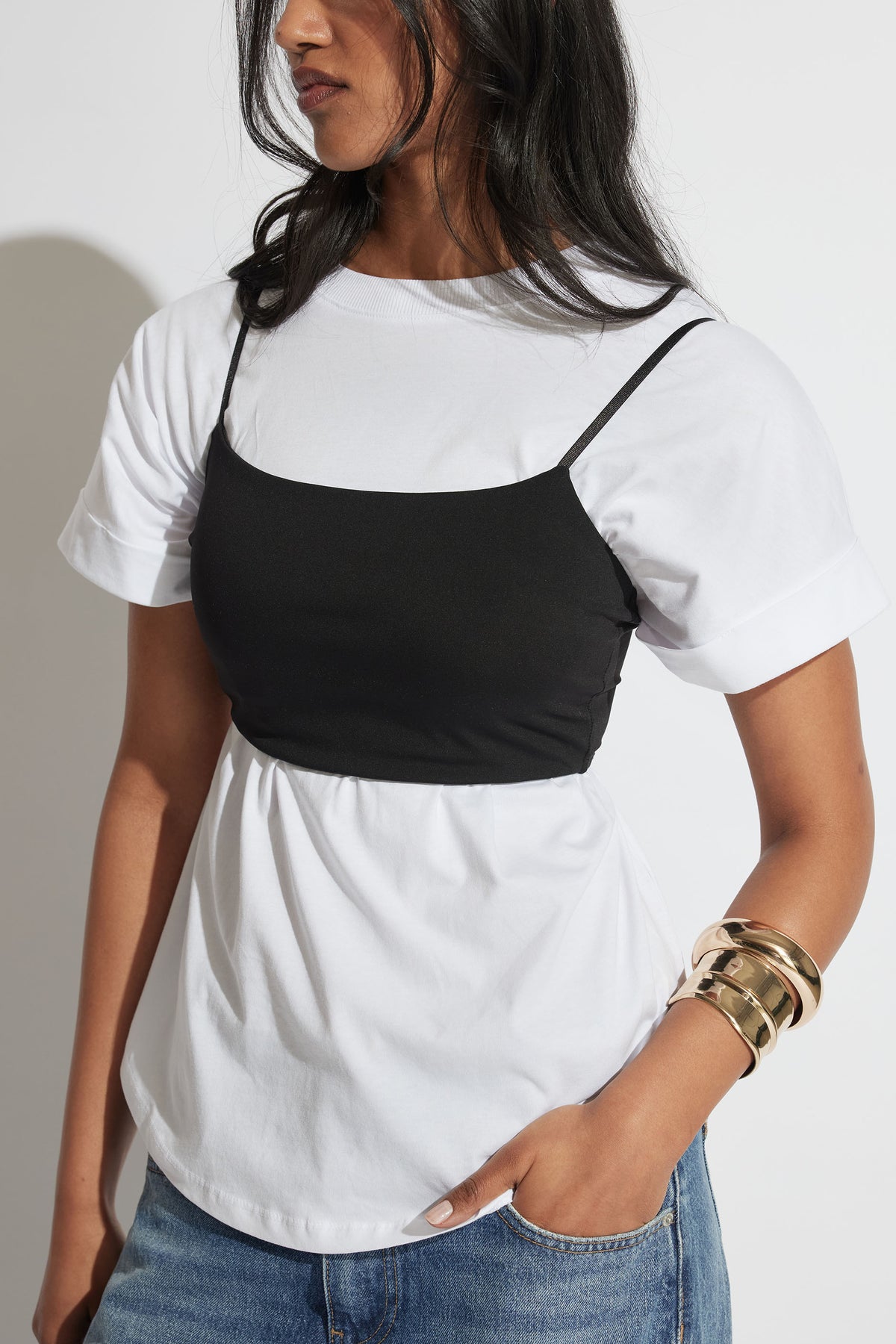 Woman wearing a black fitted crop top over a white T shirt with blue jeans