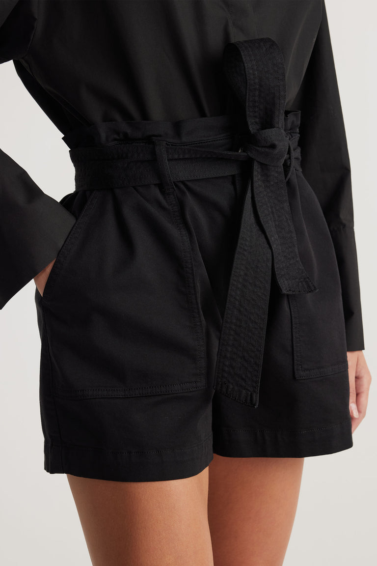 Close-up of woman wearing black high-waisted shorts with a tied belt and large front pockets styled with a long-sleeve top