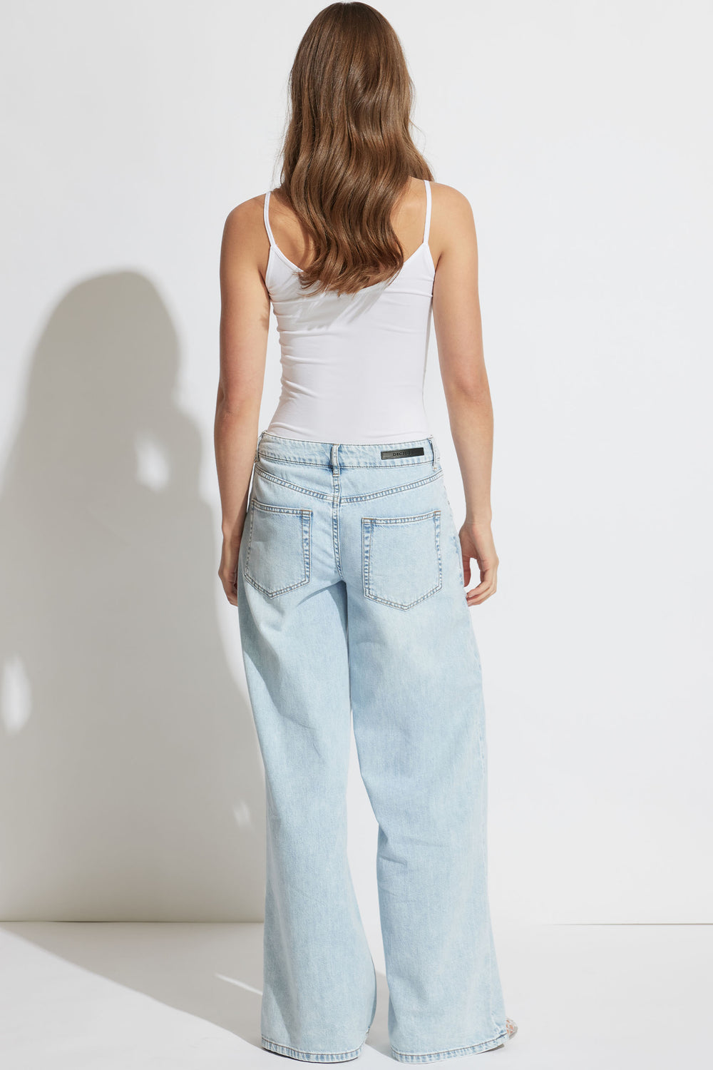 Woman wearing a white thin strap tank top paired with relaxed light wash wide-leg denim jeans, shown from back