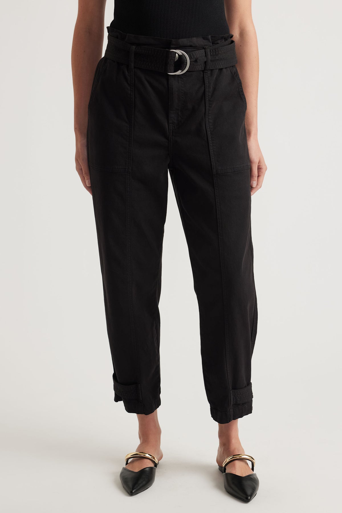 Front view of black high-waisted pull-on pants with belt and cuffed hems paired with pointed flats
