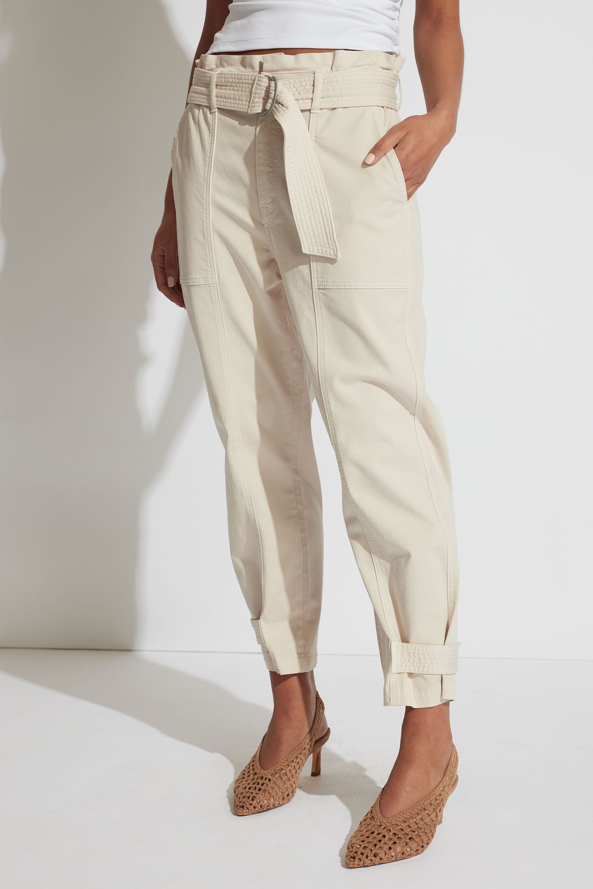 Woman wearing stone-colored belted pull-on pants with cuffed ankles paired with woven pointed heels and a white top.
