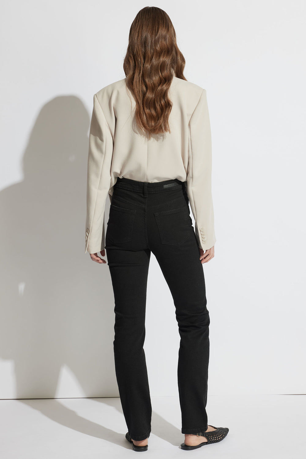 Back view portrait of woman wearing black Billie Straight Leg Jean paired with beige top, gallery position 3 in soft denim