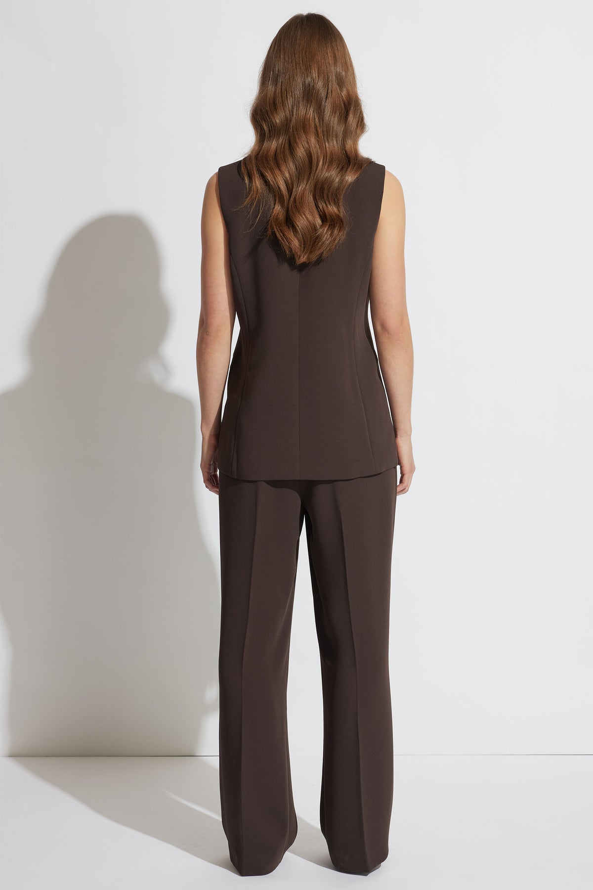 Woman shown from behind wearing a tailored dark brown vest and matching wide-leg pants with loose wavy hair