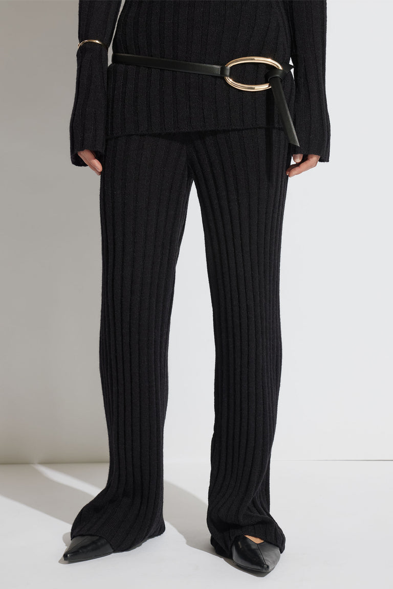 Close-up of a woman wearing black rib knit pants styled with a matching top, black belt, and pointed flats.